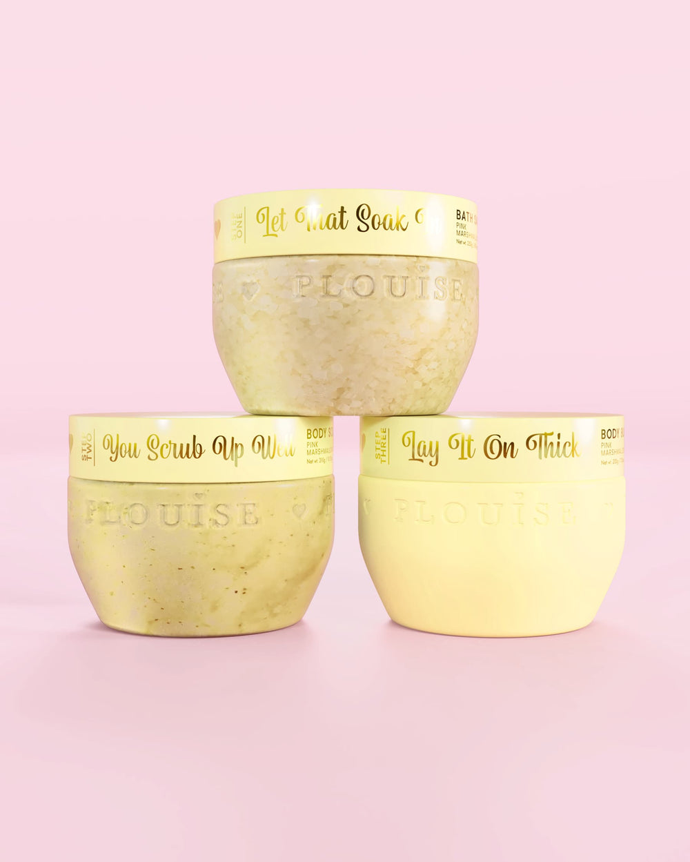 Tres contenedores amarillos de P.Louise Hop Into Self-Care Starwberry Shortcake con sales de baño, exfoliantes corporales y manteca corporal con texto dorado sobre un fondo rosa