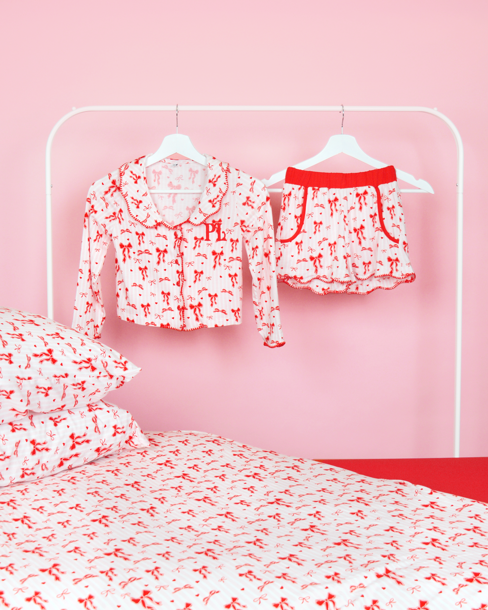Set of pink and white striped girls P.Louise Christmas bow pyjamas shorts on hangers in a pink bedroom with matching bedding