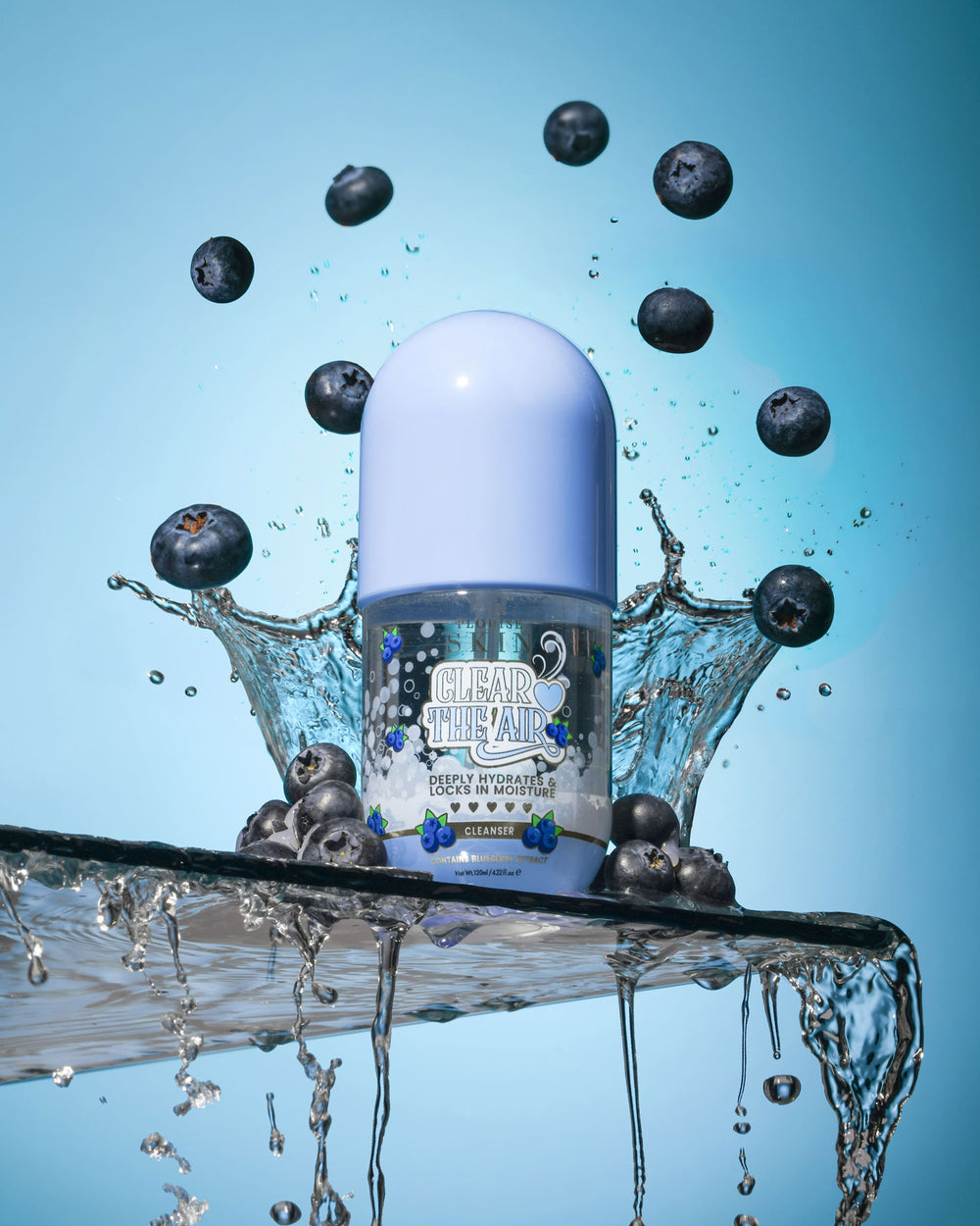 Botella de P. Louise Clear The Air Blueberry Gel Cleanserl rodeada de arándanos y salpicaduras de agua sobre un fondo azul