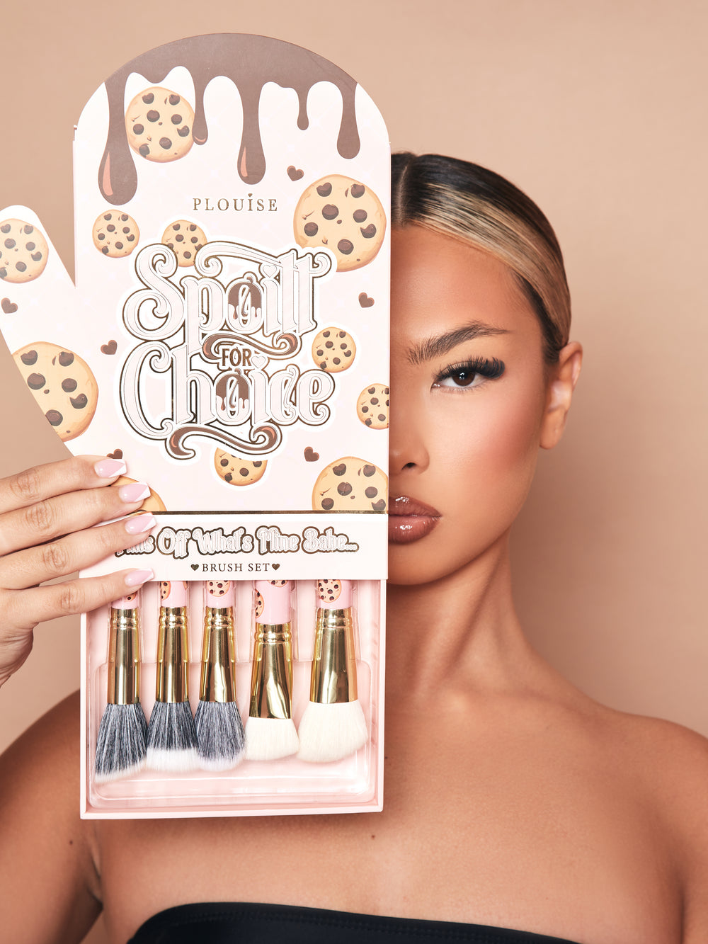 Una imagen del juego de brochas de maquillaje de 5 piezas de P.Louise Spoiled For Choice en una caja de embalaje con guantes de horno con una bandeja sacada de la parte inferior que muestra las brochas parcialmente. El paquete muestra la mitad de la cara de una modelo maquillada.