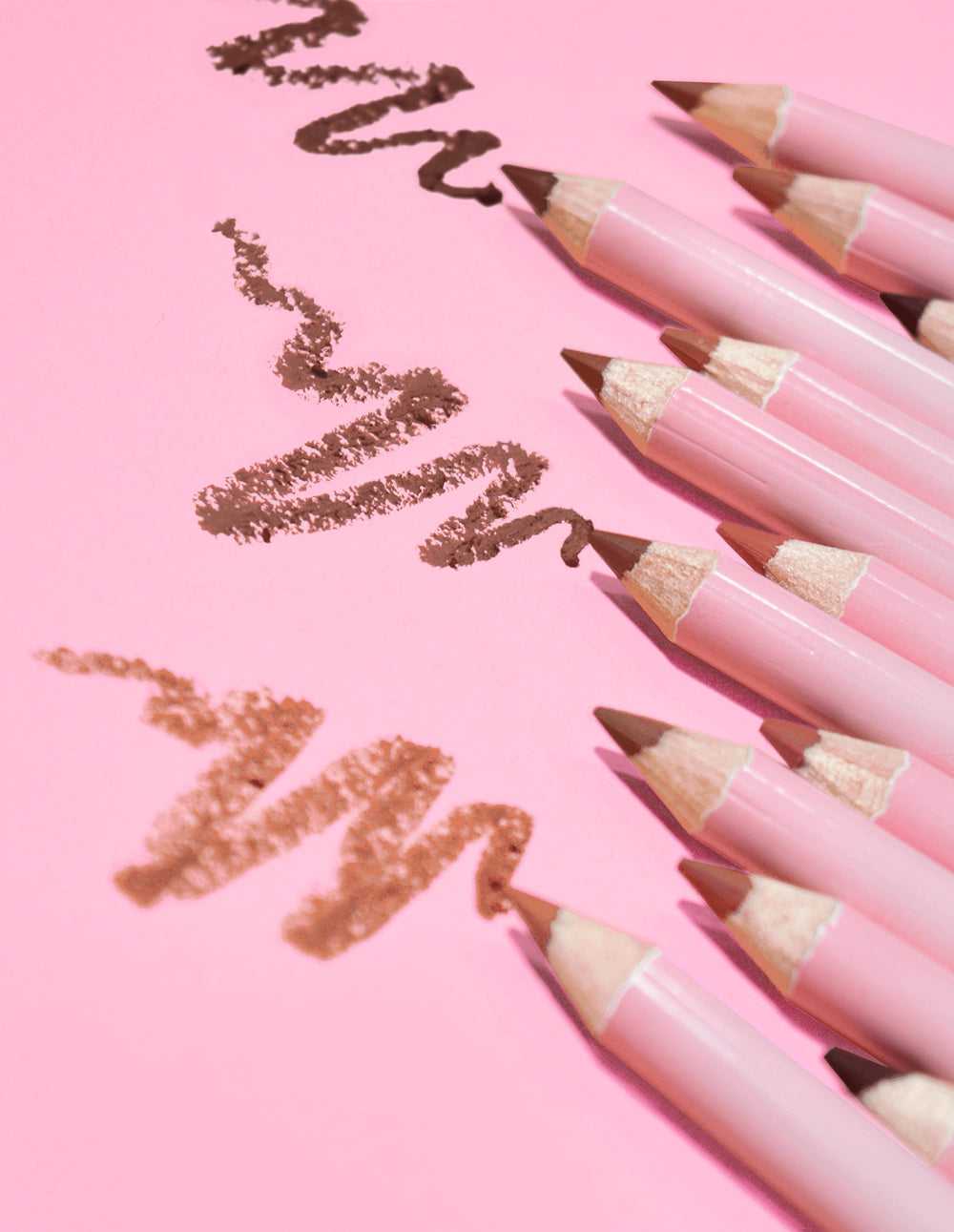 Eine Kollektion von P.Louise-Liplinern mit ultimativer Definition zum Schärfen in verschiedenen Nude-Tönen, auf einem rosa Hintergrund angeordnet, auf deren Oberfläche einige Linien des Produkts gezeichnet sind.