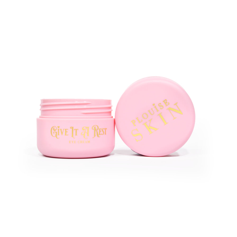 Un frasco rosado abierto de P.Louise Give It A Rest Eye Cream que muestra la tapa y el frasco desde el costado con la marca y el nombre del producto en el frasco con letras doradas.