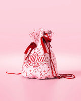 Rosa Kordelzugtasche mit roten Schleifen und festlichem Design mit „P.Louis“-Branding auf rosa Hintergrund