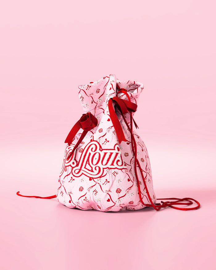 Bolso rosa con cordón, lazos rojos y diseño festivo con la marca 'P.Louis' sobre fondo rosa