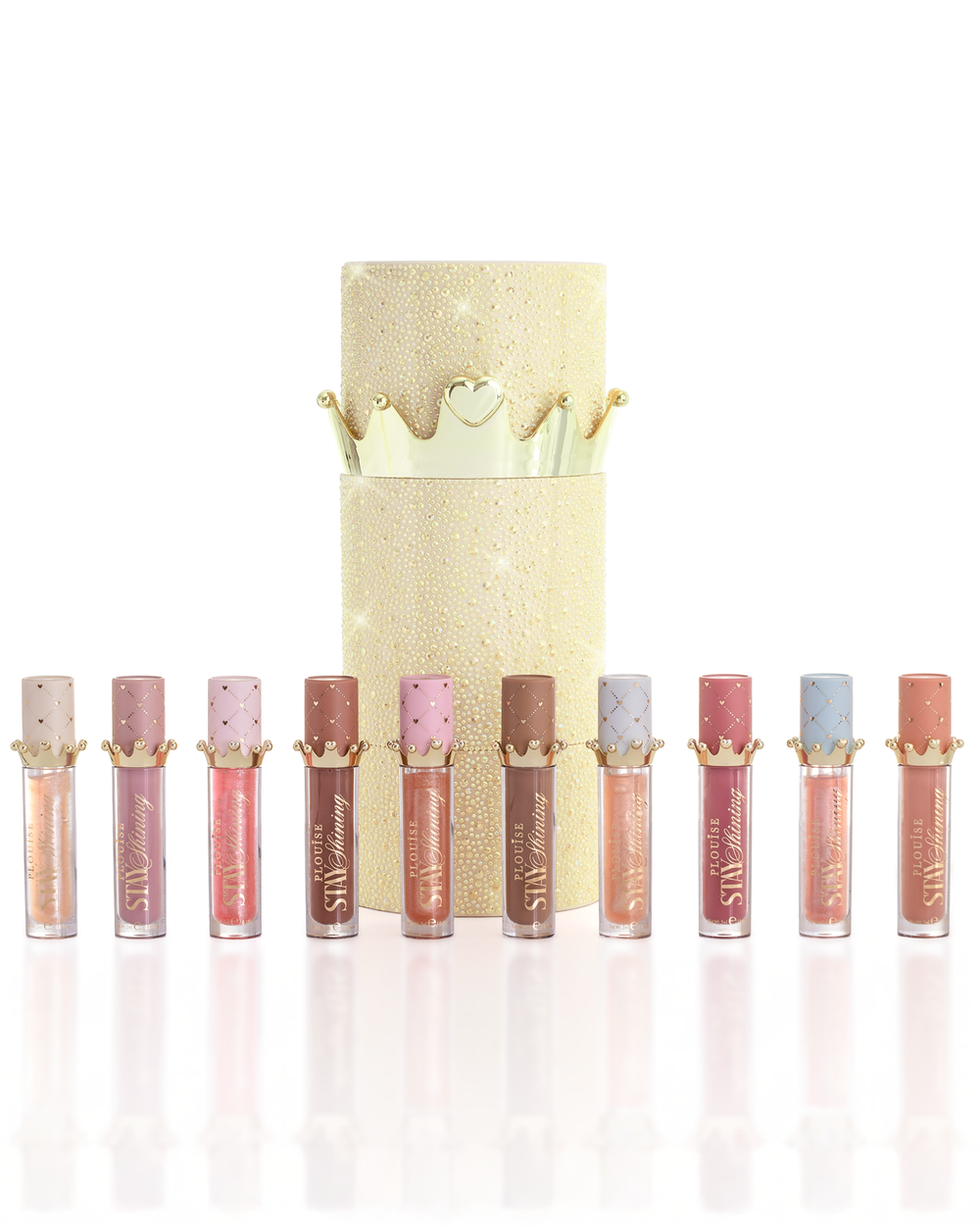 Un conjunto de diez productos de aceite para labios P.Louise Christmas Stay Shining dispuestos en fila frente a una caja de aceite para labios cilíndrica dorada brillante con una tapa de corona dorada, sobre un fondo blanco limpio.