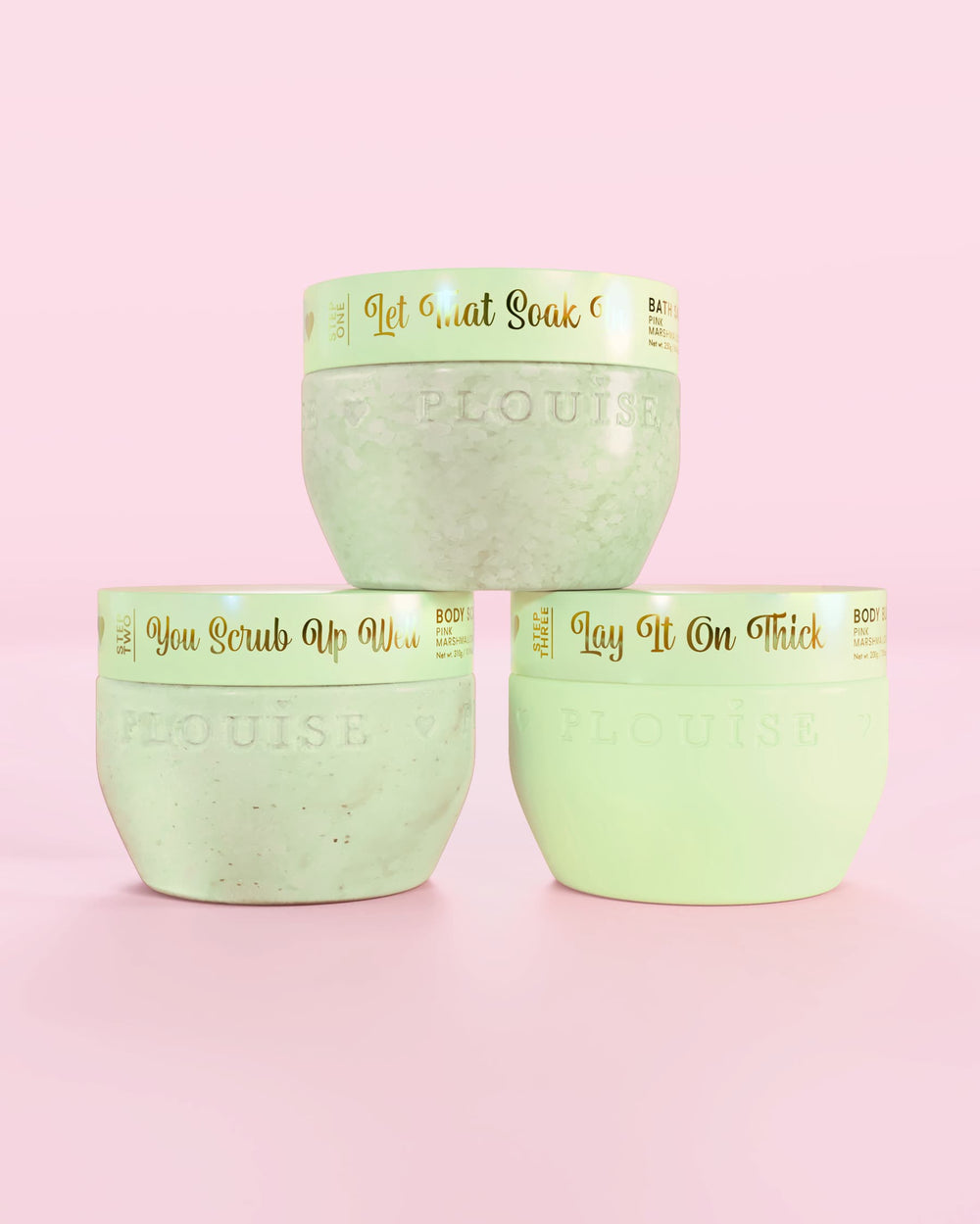 Tres contenedores verdes de fresas cubiertas de chocolate P.Louise Hop Into Self-Care con sales de baño, exfoliantes corporales y manteca corporal con texto dorado sobre un fondo rosa