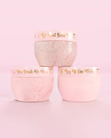 Tres recipientes rosas P.Louise Hop Into Self-Care Pink Marshmallow con sales de baño, exfoliantes corporales y manteca corporal con texto dorado sobre un fondo rosa