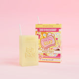 Ein gelbes Stück Seife mit der Gravur „Bad Bitch“, begleitet von einer bunten Saftschachtel mit der Aufschrift „Fizzy Pop“, präsentiert auf einem rosa Hintergrund.