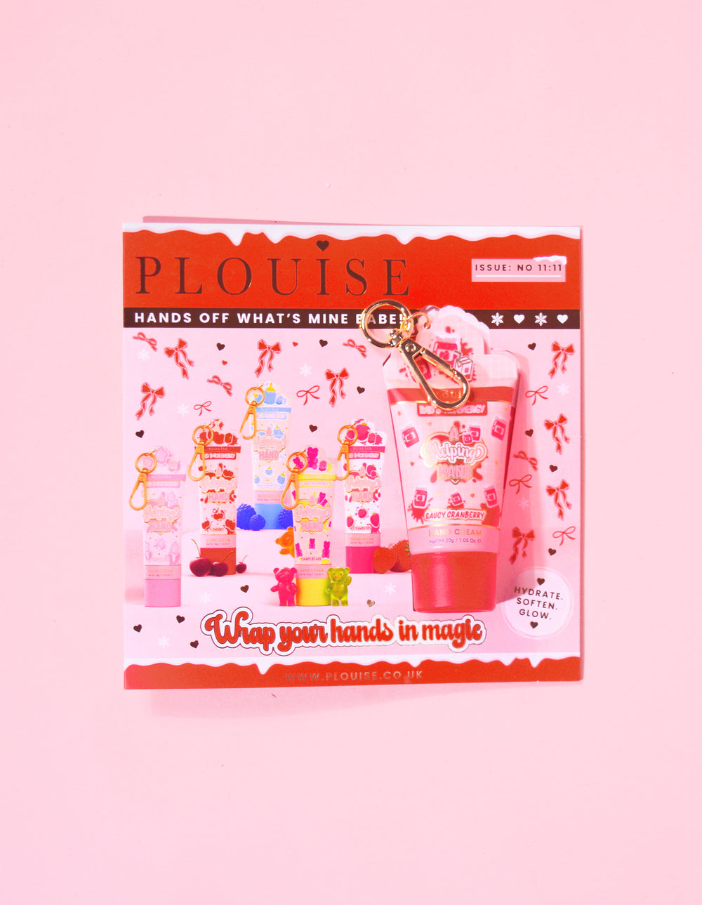 Revista navideña de P.Louise con un mini llavero con crema de manos de arándanos adjunta a la revista con un diseño festivo rojo y rosa.