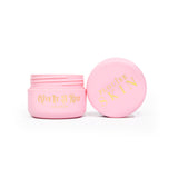 Un frasco rosado abierto de P.Louise Give It A Rest Eye Cream que muestra la tapa y el frasco desde el costado con la marca y el nombre del producto en el frasco con letras doradas.